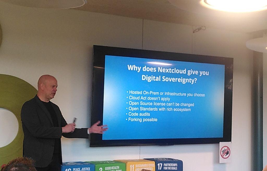 A man presenting slides in front of an audience. The slides on the screen say: “Why does Nextloud give you Digital Sovereignty? Hosted On-Prem or infrastructure you choose. Cloud Act doesn’t apply. Open Source license can’t be changed. Open Standards with rich ecosystem. Code audits. Forking possible.”